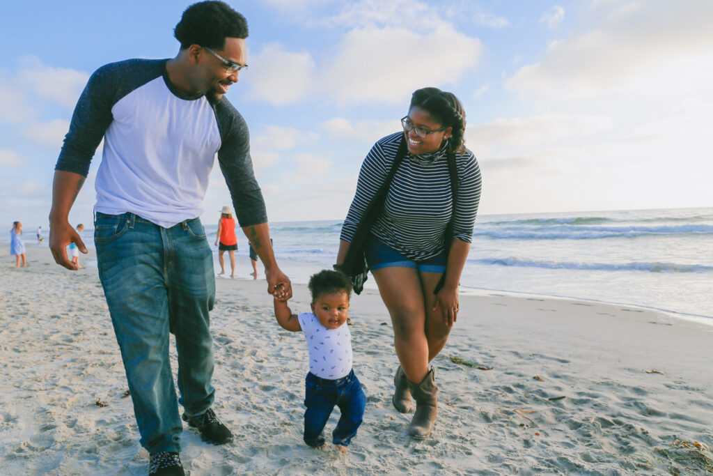 Husband and wife walking with their young son along a beach.