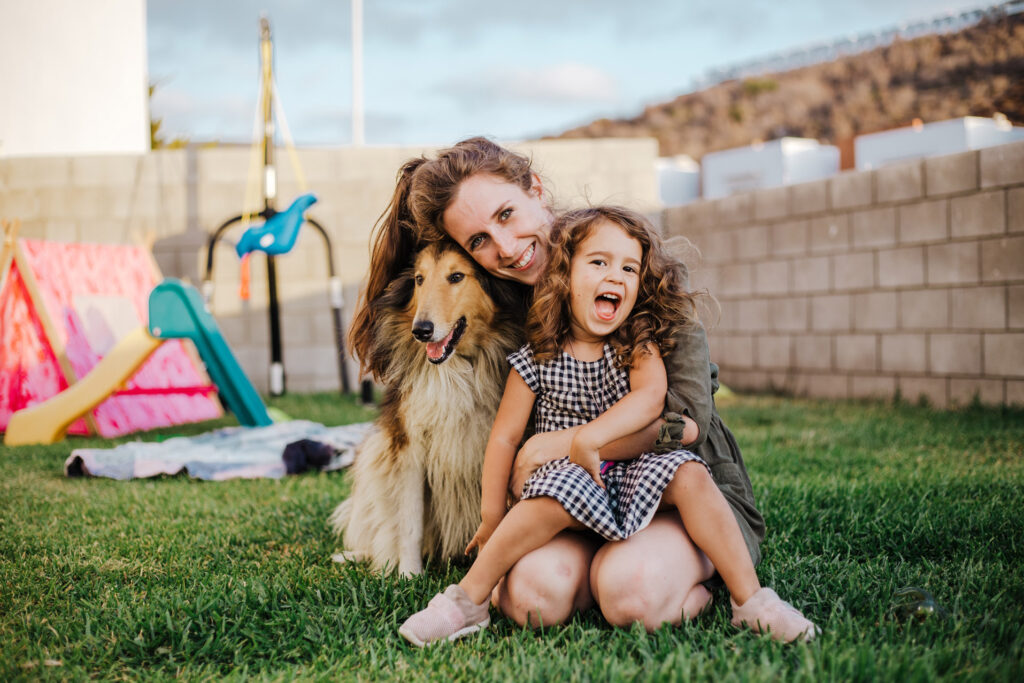 Mother sitting in her backyard with her dog and has her daughter sitting on her lap