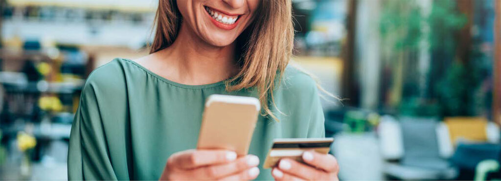 woman smiling at her phone as she takes out her credit card