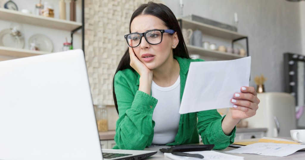 stressed woman holding a bill and looking at her computer