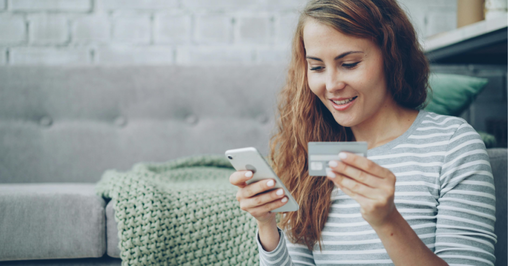 A woman holding her credit card and looking at her cell phone